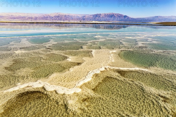 Dead Sea. The green water of the salty sea is surrounded by pink mountains. Evaporated salt forms bizarre patterns on the water. Sunny winter day. The picture was taken by a drone from a aerial view. Israel