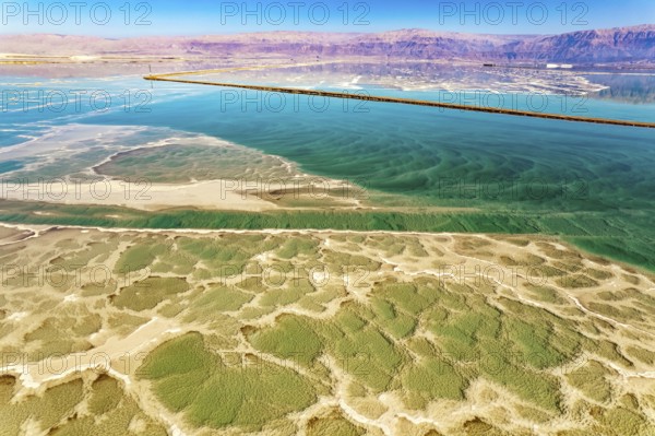 Salt deposits are visible on the seabed. Magic of the Dead Sea. The clear green water of the salty sea is surrounded by pink mountains. The photo was taken from a drone. Cold sunny day. Israel