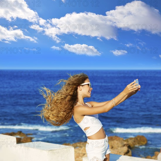 Blond kid teen girl photo selfie on smartphone in a beach at Mediterranean