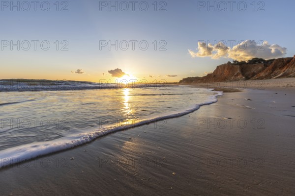 Beautiful sandy beach with red rocks and cliffs. Twilight at sunset with shallow waves on the Atlantic coast in Praia do Poço Velho, Praia da Falésia, Algarve, Portugal, Europe