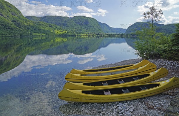 Yellow kayaks on the shore, mountain range reflected in Lake Bohinj, Triglav National Park, Julian Alps, Gorenjska region or Upper Carniola, Slovenia, Europe