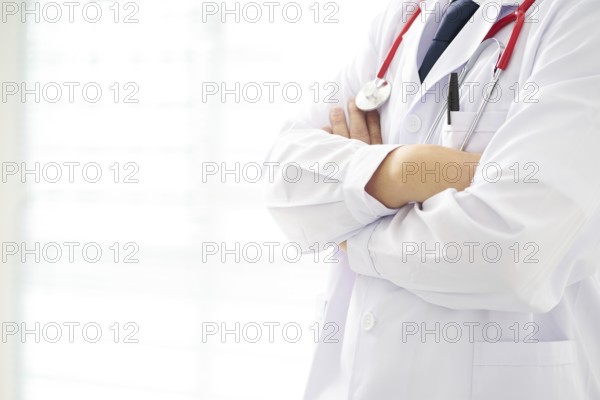 Unknow doctor posing with arms crossed in the office, he is wearing a stethoscope
