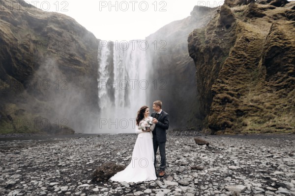 Wedding couple near Skogafoss waterfall. Destination Iceland wedding. The groom hugs the bride by the shoulders, they laugh together