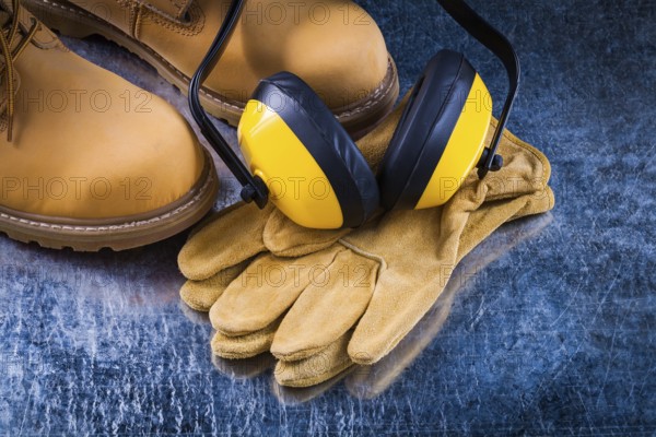 Leather safety boots gloves and noise insulation ear muffs on scratched metallic background construction concept