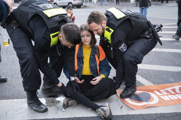 28.04.2023, Berlin, Germany, Europe, Climate demonstrators of the so-called Last Generation stick to the carriageway of a main road at Ernst-Reuter-Platz in Berlin-Charlottenburg and cause severe traffic obstructions while officers of the Berlin police carry one of the activists off the road. The activists' main demands are an affordable 9-euro ticket for everyone and a general speed limit of 100 km/h on German motorways. The group is also calling on the German government to take more drastic measures to reduce greenhouse gas emissions and to phase out the use of all fossil fuels by 2030, as well as calling for a social council, Europe