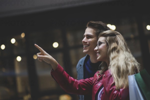 Beautiful couple with shopping bags is talking and smiling while doing shopping in the mall focus on the woman
