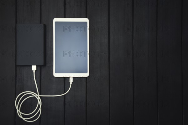 Power bank loads tablet PC, smartphone, isolated on wooden background. charging concept. free copyspace