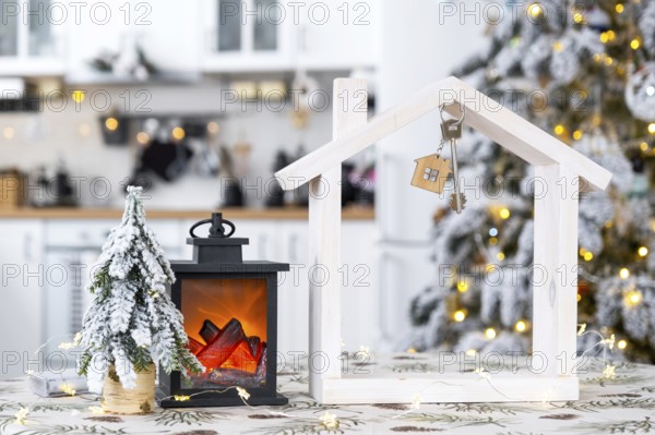 Key and tiny house of a small size on cozy home with Christmas decor on table of festive white kitchen. Gift for New Year. Insurance, moving to new house, mortgage, rent and purchase real estate