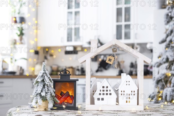 Key and tiny house of a small size on cozy home with Christmas decor on table of festive white kitchen. Gift for New Year. Insurance, moving to new house, mortgage, rent and purchase real estate