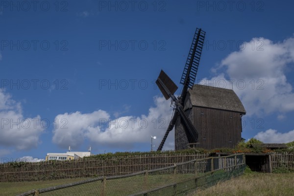 Germany, Berlin, 19.09.2023, Marzahner Bockwindmühle, a trestle windmill in Berlin-Marzahn, the name of the mill type says it all: the mill house stands vertically on a single thick beam, the house tree, which ends just above the ground. The house beam is supported by a four-footed trestle. This allows the mill, which is more than 14 metres high, to be rotated through 360 degrees. Wooden bollards are placed around the mill. They mark the minimum distance so that nobody is hit by the rotating wind blades, which have a span of around 20 metres. 01, Europe