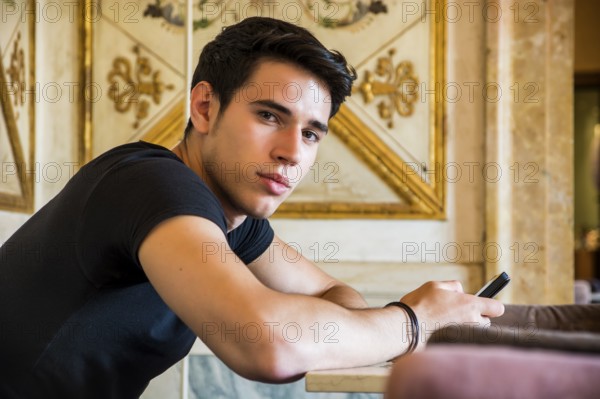 Young handsome man sitting in elegant cafeteria or restaurant using cell phone to send text message
