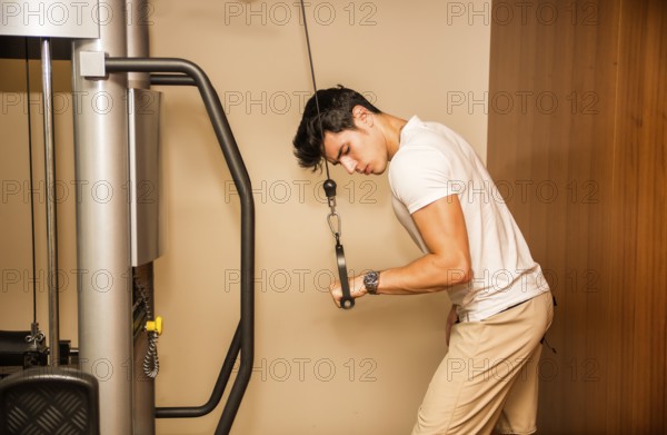 Attractive and fit young man in gym working out, doing pulley and exercising triceps on equipment
