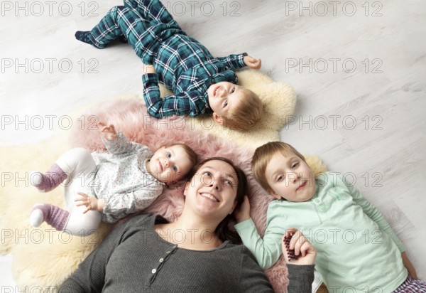 Top view of a beautiful young mother, her sweet little daughter and her two sons smiling at the camera and lying on the wooden floor