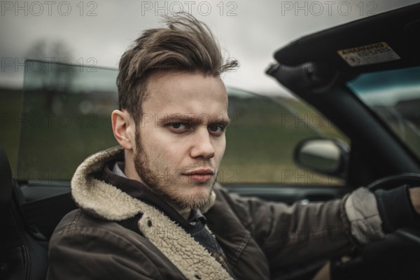 A serious-looking man driving a convertible in the countryside