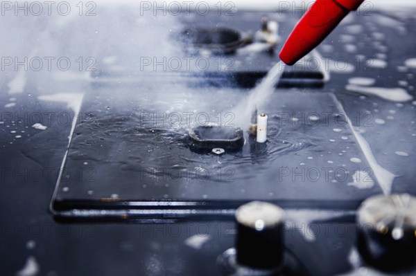 Focused image of water being sprayed from a red nozzle onto a stove