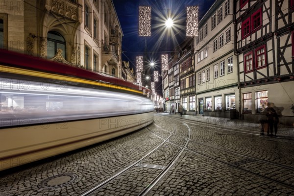 Langzeitbelichtung einer Straßenbahn, die durch eine historische Straße mit Fachwerkhäusern fährt, Erfurter Weihnachtsmarkt Erfurt