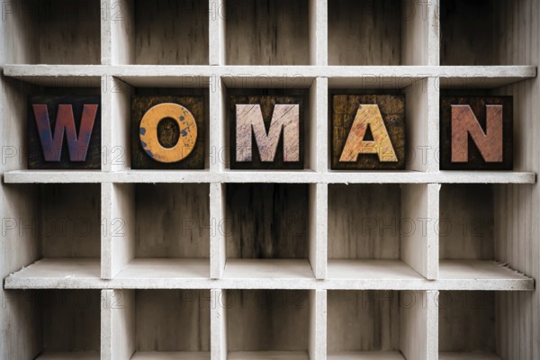 The word WOMAN written in vintage ink stained wooden letterpress type in a partitioned printer's drawer
