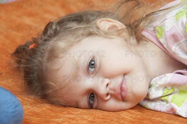 Cheerful three year old girl lying on the bed and looked into the frame