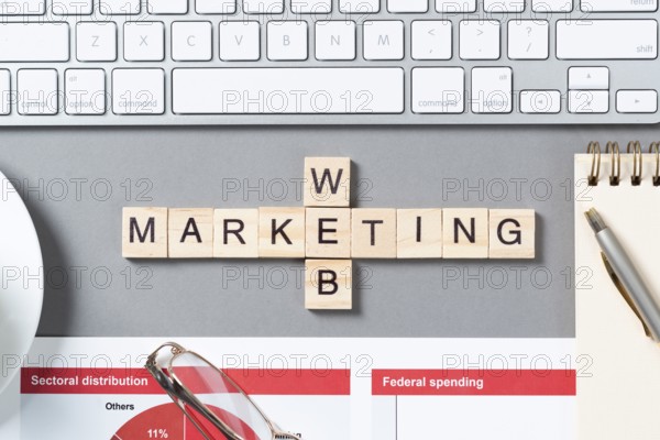Web marketing concept with letters on cubes. Still life of office workplace with crossword. Flat lay grey surface with pc keyboard and cup of coffee. New strategy planning and workflow optimization