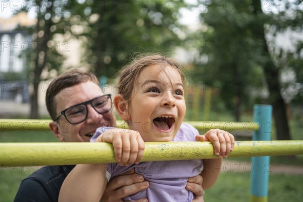 Father with child girl doing pull-ups on workout outdoor area. Healthy active lifestyle, happy family time. Modern fatherhood concept .