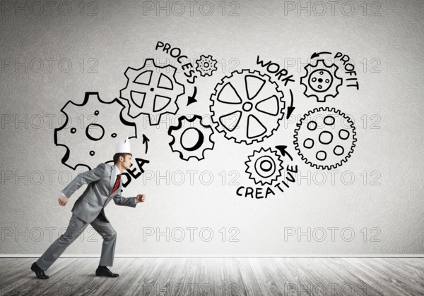 Young handsome businessman wearing white paper crown running and gear mechanism on wall