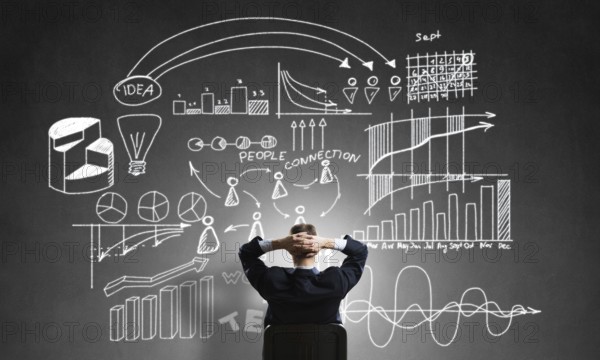 Rear view of businessman sitting in office chair and looking at infographs on chalkboard