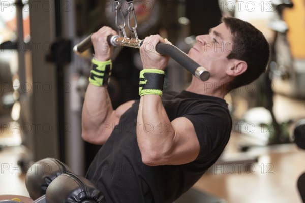 Cheerful guy training dorsal muscles by taking handles and bringing them down. Strength exercising concept