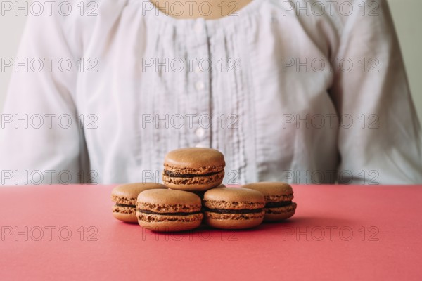 Macaroons on heap on pink table against woman. Selective focus