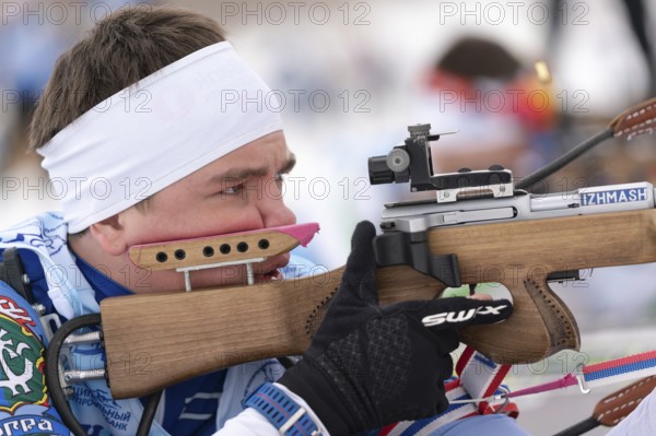 Close-up view of sportsman biathlete aims rifle shooting prone position. Biathlete Andrey Krutov in shooting range. Regional youth biathlon competitions East Cup. Kamchatka, Russia, April 12, 2019, Europe