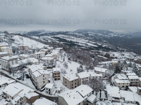 Aerial view of snow-covered houses and trees in bore, a small village nestled in the hills surrounding parma, italy, during a winter snowfall in december 2024