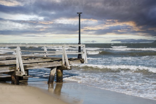 Storm sea waves empty wooden pier in dramatic blue sky background. Seascape with running splashing sea waves. Sandy beach vacation getaway in Gdansk Poland. Copy space for your text