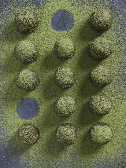 Bliss balls or energy balls sprinkled with matcha green tea. Placed in a row with some round holes without powder of missing ball