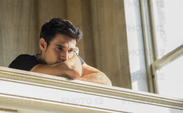 Portrait of Shy Attractive Young Man Leaning on Folded Arms Against Polished Marble Staircase Railing Inside Classical Building