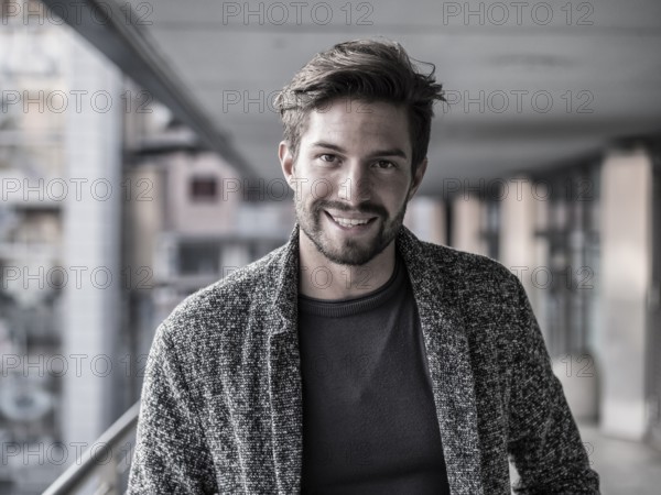 One handsome young man in urban setting in European city, standing and smiling to camera happy