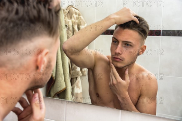 Handsome man looking at his face in mirror, checking hair and hairline