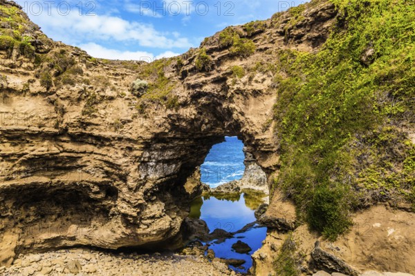 Small puddle of water in an arch. Coastal rocks formed a picturesque arch of sandstone. Great Ocean Road of Australia. The concept of exotic, active and photo-tourism