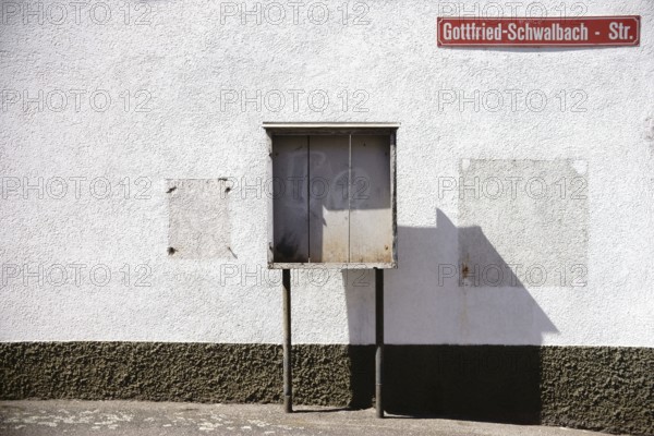 A vintage wooden display case stands on the façade of a building on the wall of which a cigarette machine and wooden frame have been dismantled