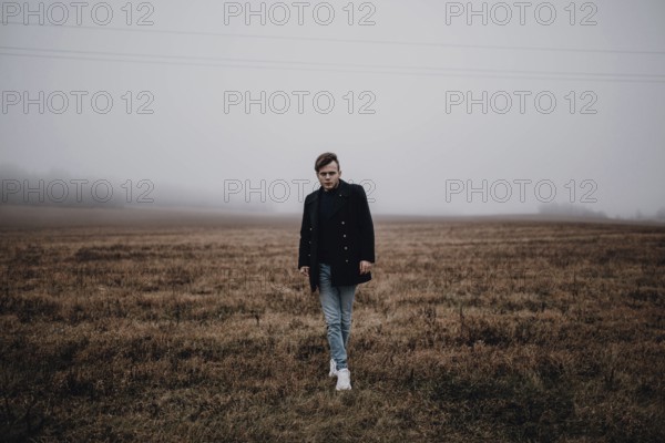 A man in a coat stands in a foggy field, evoking a moody, autumnal atmosphere