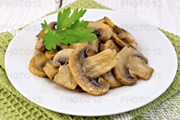 Champignons fried in a plate with a leaf of parsley on a napkin on the background light wooden boards