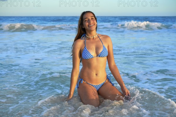 Latin beautiful bikini girl happy sitting in Caribbean beach sunset