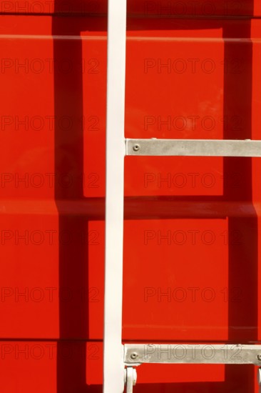 Close-up of the body of a fire engine in the sunshine with a ladder casting a shadow