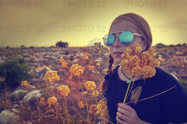 Blond country girl with sunglasses and flowers at sunset outdoor mountain