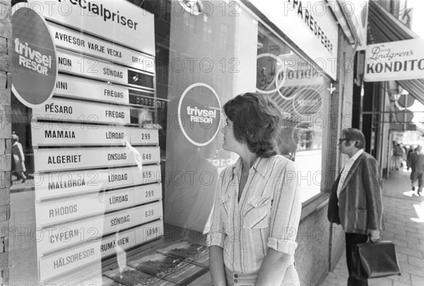 In the shop window of a travel agency. A woman is seen looking at the sign and information of the special prices for charter and package holidays to different destinations in the sunny part of south of Europe. 1975 Kristoffersson ref DV21