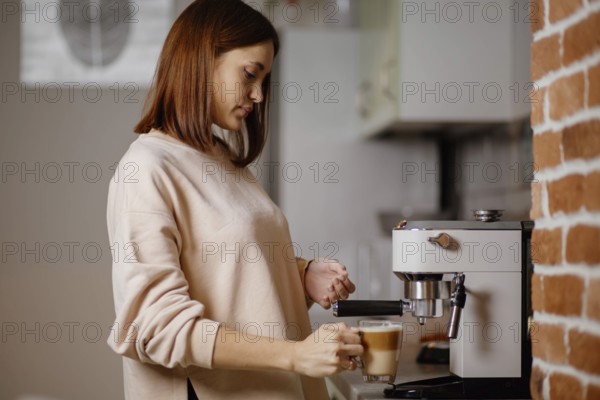 Woman adding milk to coffee using an espresso machine in the kitchen
