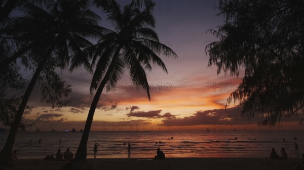 Silhouetted people and palms near sea. Sunset at tropical White beach, Boracay island, Philippines, Asia