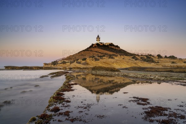 A view of the Cabo de la Huerta lighthouse at sunrise with reflections in tidal pools in the foreground