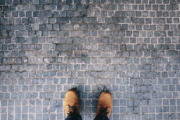 Male feet in brown boots stand on the cobblestones. Close-up.