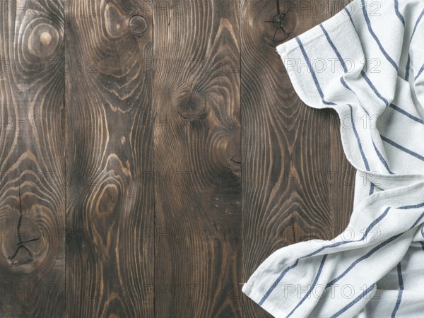 View from above on brown wooden table with linen kitchen towel or textile napkin. Blue tablecloth on dark brown wood tabletop. Copy space for text. Can use as mock up for design