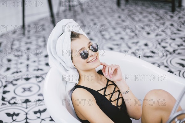 Young caucasian woman with towel on head and sunglasses getting spa treatment in a beauty salon, inside an interior room. Relaxing in the bathroom in linen. The concept of body care and relaxation