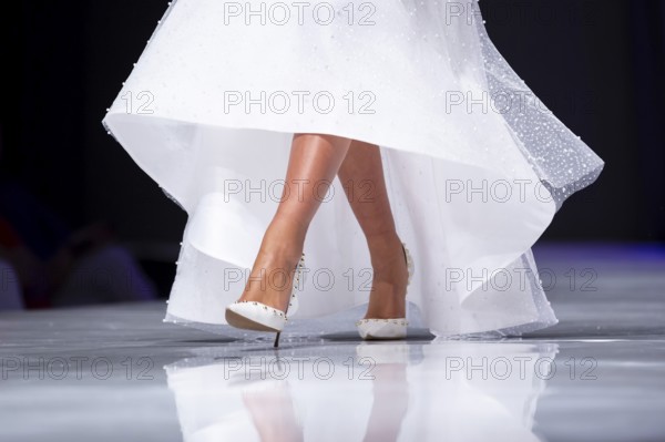 Female model walks the runway in white dress during a Fashion Show. Legs and shoes only. Fashion catwalk event showing new collection of clothes. Single female model in beautiful dress